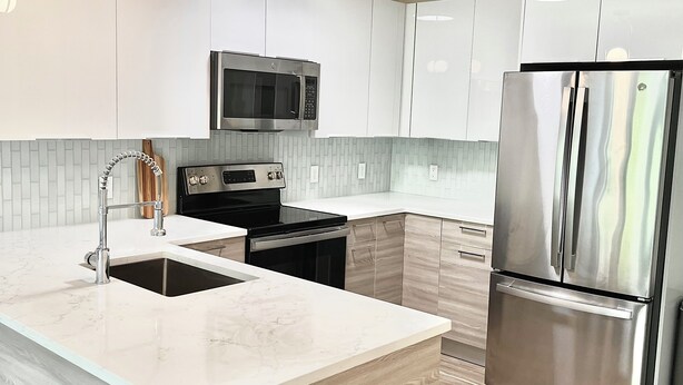 Una cocina moderna con armarios blancos, un refrigerador de acero inoxidable, un microondas y un lavamanos con un grifo moderno.