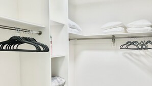 Un armario vestidor blanco con estantes y espacio para colgar, suelo de madera y una lámpara en el techo.