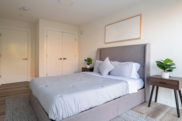 Ein Schlafzimmer mit einem Bett, Nachttischen, einer Topfpflanze und einem gerahmten Bild an der Wand.