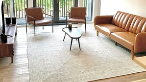 Un salón amplio con un sofá de cuero marrón, dos sillones, una mesa de centro y un ventanal con balcón.