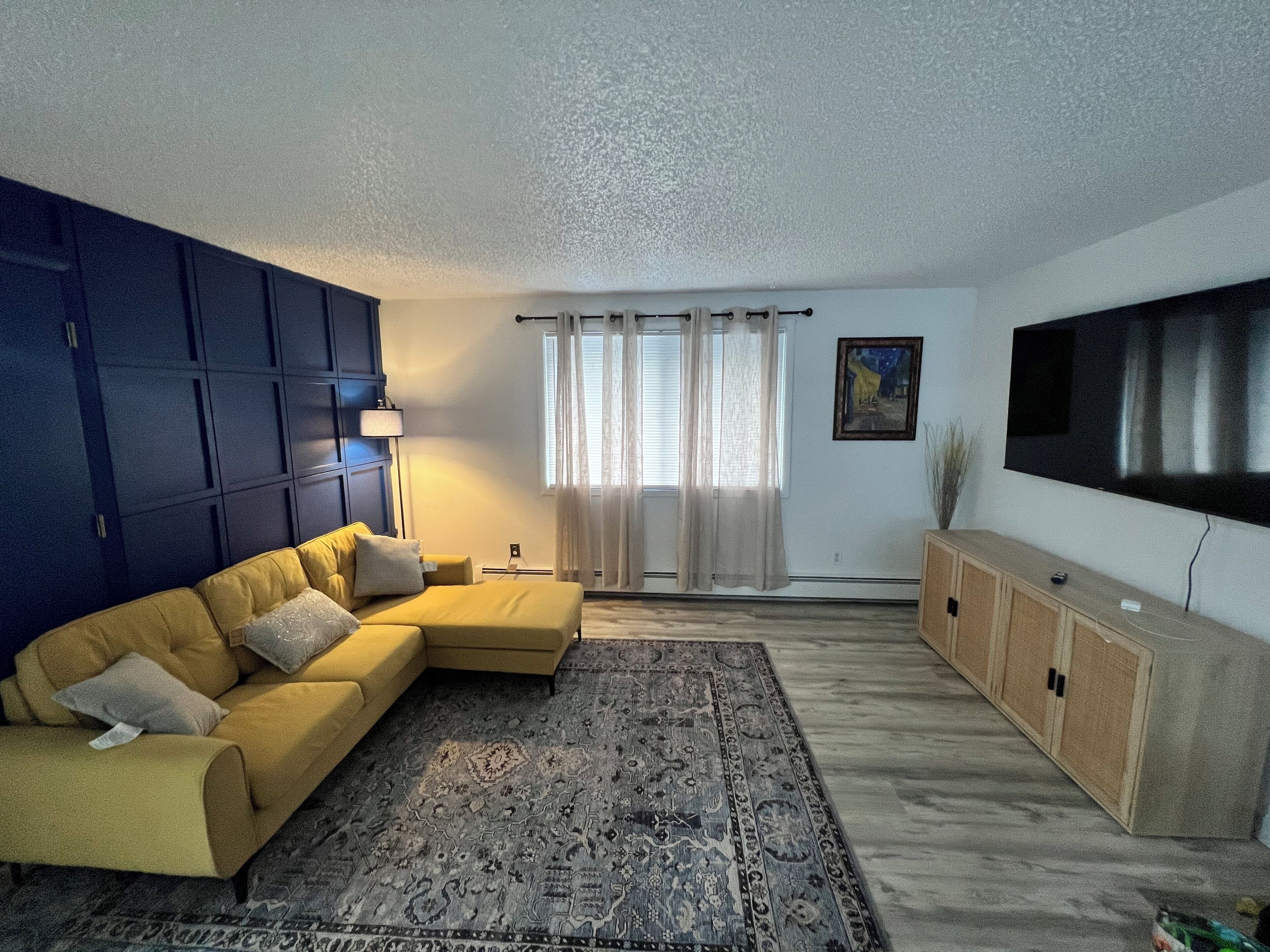 Una sala de estar con un sofá modular, un tapete estampado, un televisor de pantalla plana y un mueble.