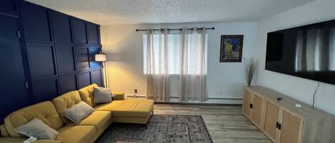 Una sala de estar con un sofá modular, un tapete estampado, un televisor de pantalla plana y un mueble.