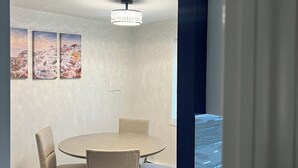 Ein moderner Essbereich mit einem runden Tisch, vier Stühlen, einer Chandelierleuchtre und drei gerahmten Kunstwerken an der Wand.