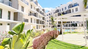 A modern multi-story residential building with balconies, a swimming pool, and a well-maintained garden. - Ático Marina Real III (Dénia)