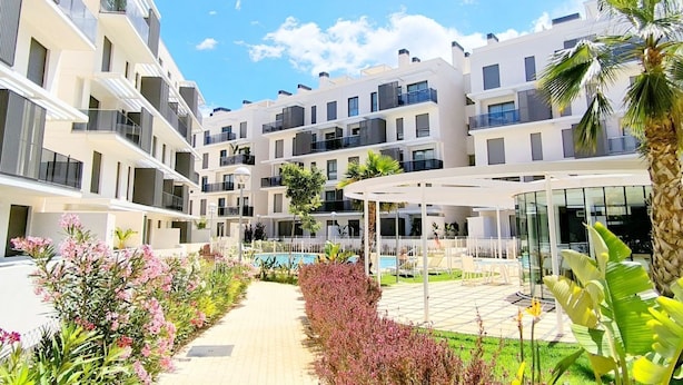 A modern multi-story residential building with balconies, a swimming pool, and a covered outdoor seating area. - Ático Marina Real III (Dénia)