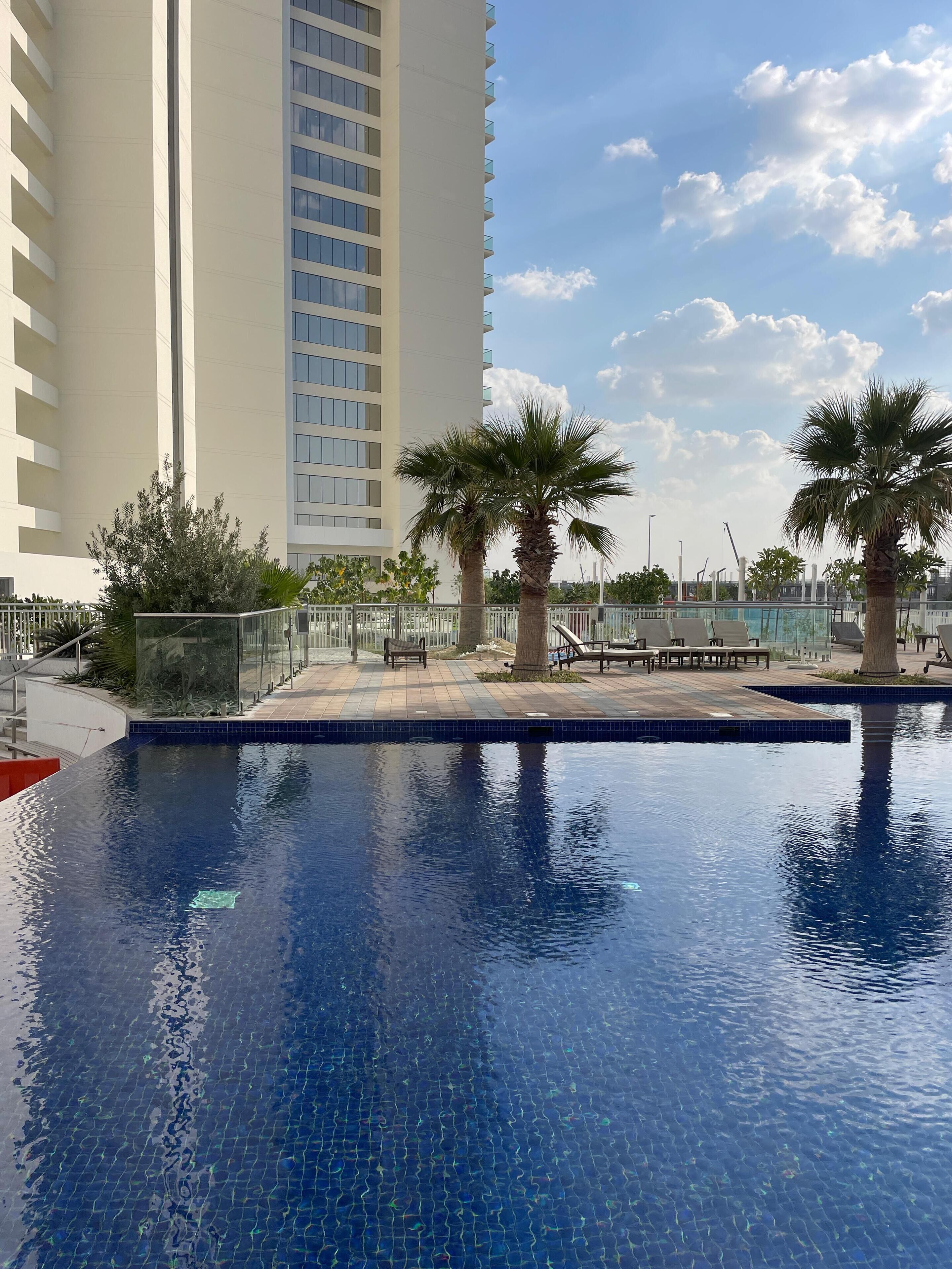 A swimming pool with a tiled edge, surrounded by palm trees and benches.