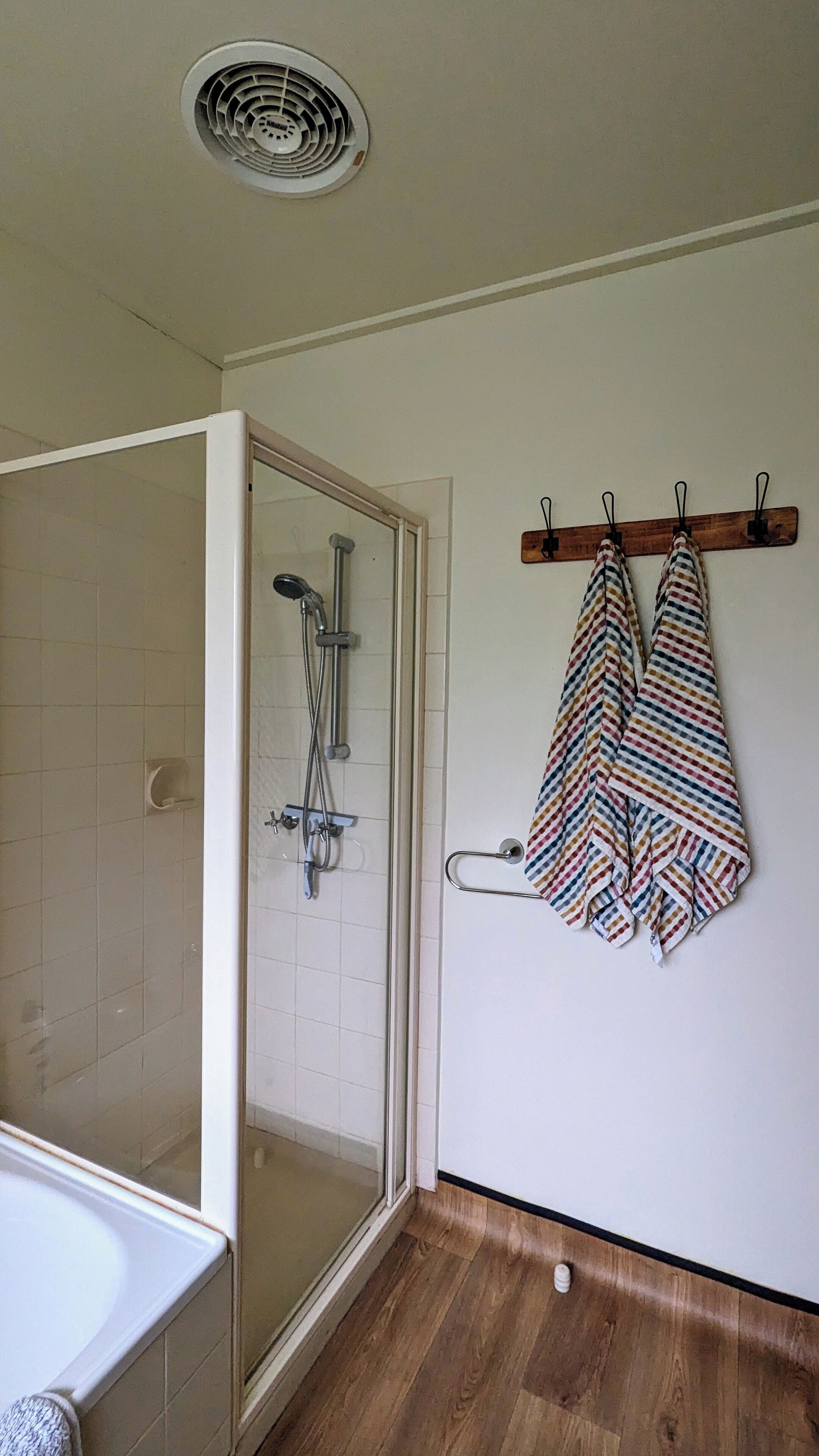 Een badkamer met een douche, een handdoekhouder met handdoeken en een ventilatie rooster in het plafond.