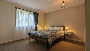 A bedroom with a bed, two bedside lamps, a window with curtains, and a hanging light fixture. - Al'May Rawson escape, family cottage.
Entire Home in Rawson, Australia  (Rawson)