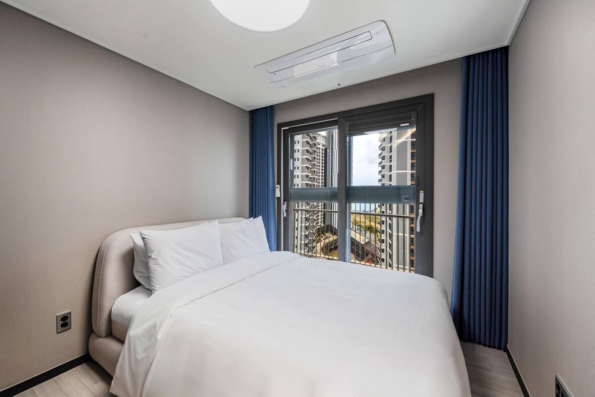 Una habitación de hotel con una cama, un ventanal con cortinas azules y vistas a rascacielos.