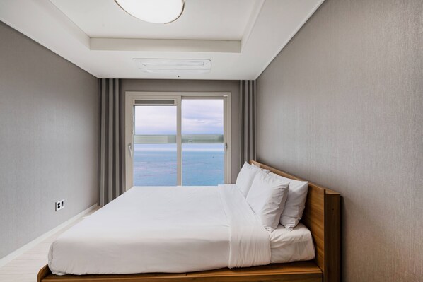 A bedroom with a large bed, a view of the sea through a sliding door, and a ceiling light. - Odays Osiria Residence (Busan)
