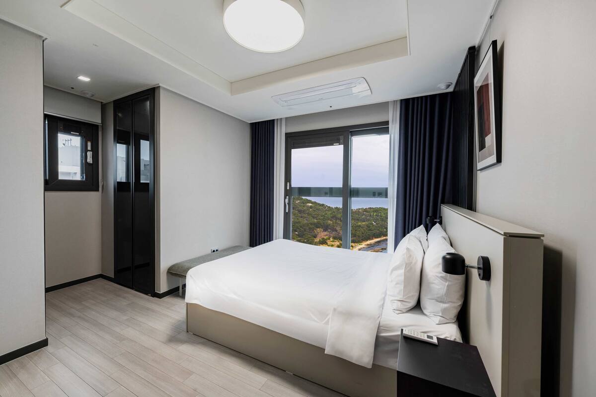 Una habitación de hotel moderna con una cama grande, un escritorio, vistas al exterior y una puerta corrediza a un balcón.