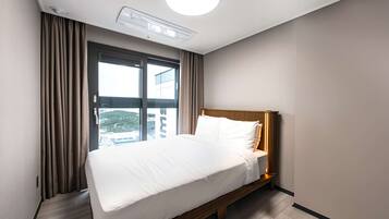 A hotel room with a bed, a window with curtains, a ceiling light, and a view of buildings outside.