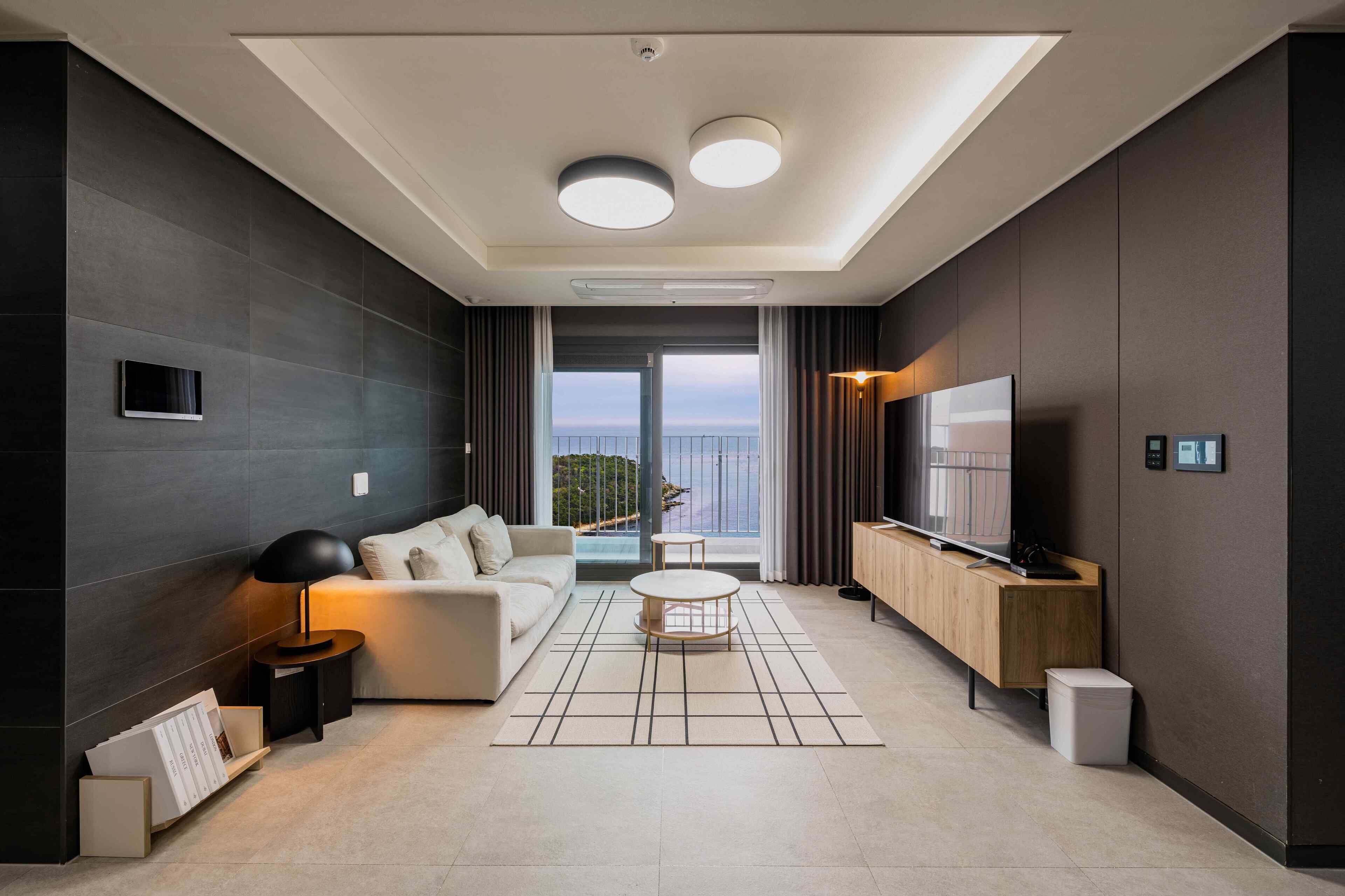 A modern living room with a sofa, coffee table, TV, and a view to the outdoors.
