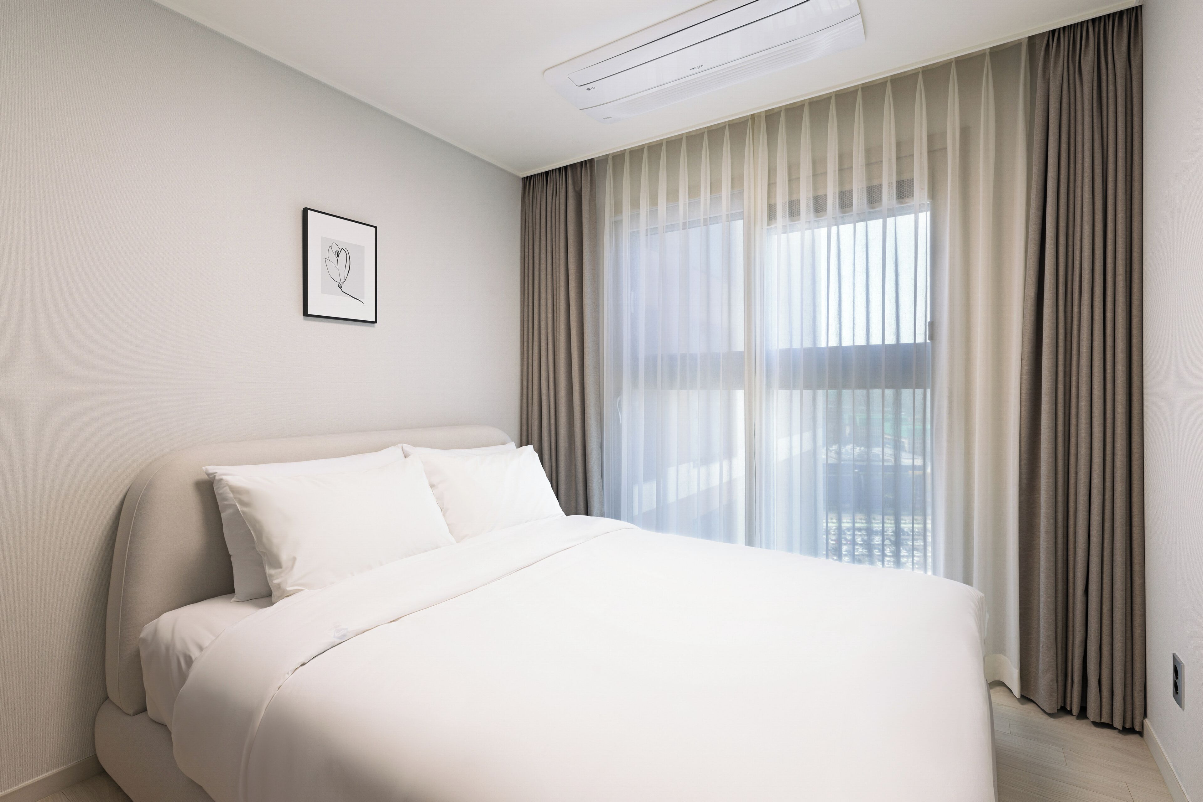 A modern hotel room with a large bed, a window with sheer curtains, and a framed picture on the wall.