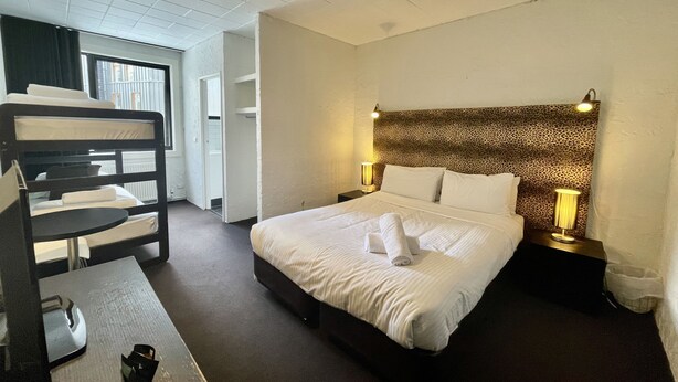 A hotel room with a bunk bed, a desk, a bed with white linens, a leopard print headboard, and bedside lamps.
