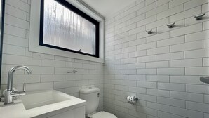 A bathroom with white subway tiles, a white toilet, a sink with a faucet, and a window above the toilet.