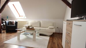 Ein Loft-Zimmer mit weißem Sofa, Glastisch und Flachbildfernseher auf einer Holdecke.