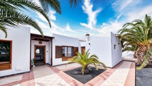 A modern building with a tiled courtyard, palm trees, and a clear sky.
