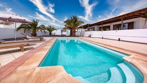 A swimming pool with lounge chairs and umbrellas, surrounded by palm trees and a clear blue sky.