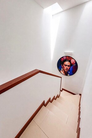 A staircase with wooden handrails and a light-colored floor, leading to a room with a circular wall decoration. - Casa Bleu - Duplex - Pool and BBQ By LVH (Puerto Calero)