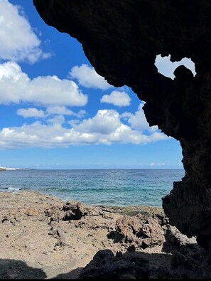 Ein felsiger Strand mit einer Höhle, die zum Meer führt, bewölkter Himmel und ruhiges Wasser.
