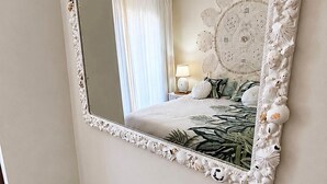 Ett sovrum med en stor spegel, en säng med ett blommigt överkast, en sänglampa och en liten pall.