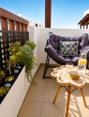 A balcony with a cushioned chair, a small table with a glass, and a planter with succulents. - Casa Bleu - Duplex - Pool and BBQ By LVH (Puerto Calero)