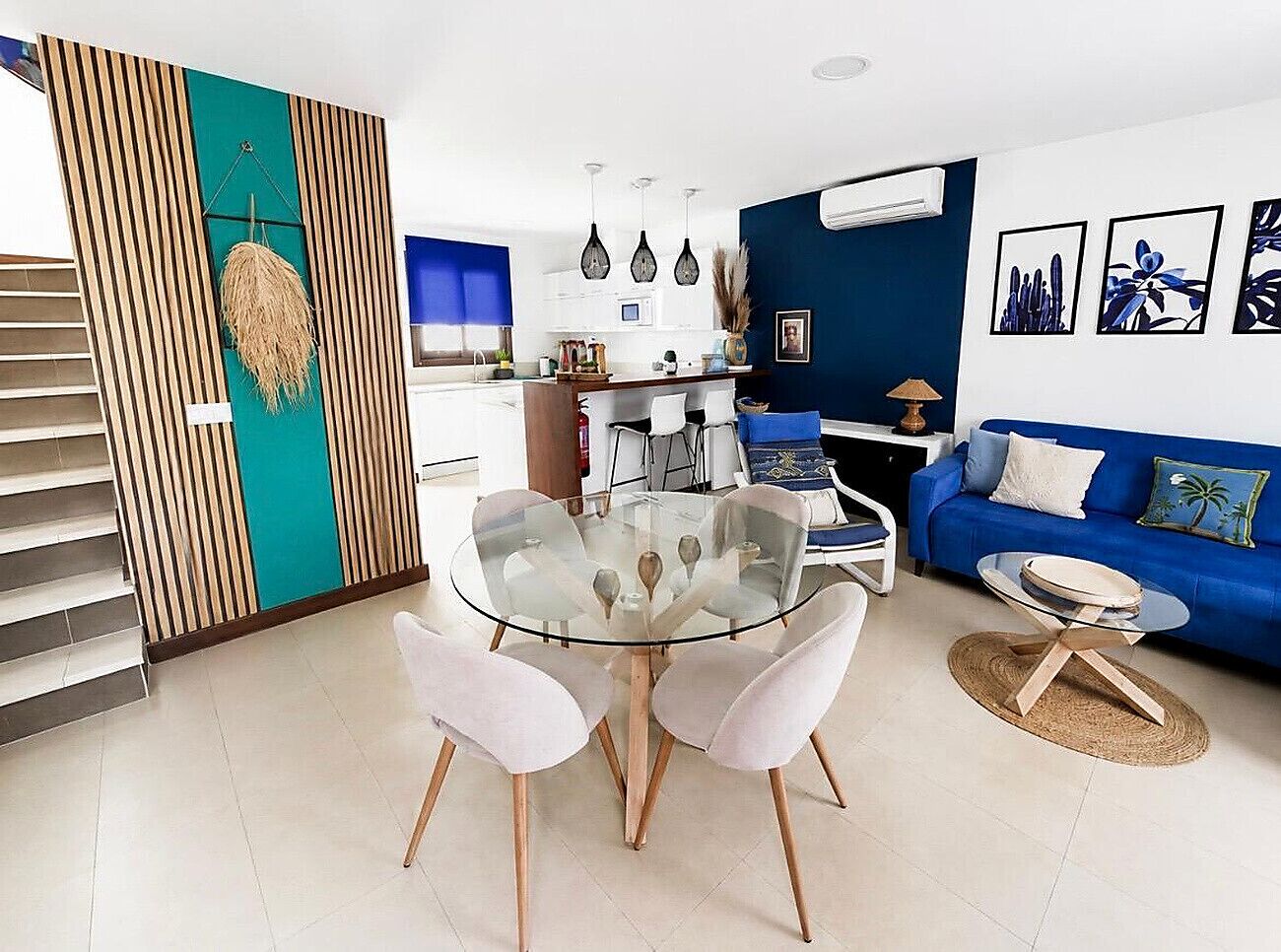 Una sala de estar moderna con una mesa de comedor de vidrio, sillas blancas, un sofá azul y una escalera.
