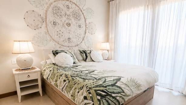 Une chambre avec un grand lit, deux tables de chevet, une tapisserie murale et une fenêtre avec des rideaux.