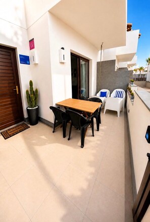 Eine Terrasse mit einem Holztisch und Stühlen, einem Topf mit einem Kaktus und einer Tür mit einem Schild.