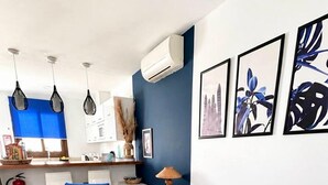 Ett vardagsrum med en blå soffa, ett runt soffbord i glas, en vit stol med en blå kudde och en liten, rund matta.