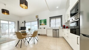 A modern kitchen with white cabinets, stainless steel appliances, and a dining area with a glass table and chairs.