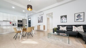 A modern living room with a black leather sofa, a glass coffee table, and a dining area with a wooden table and chairs.