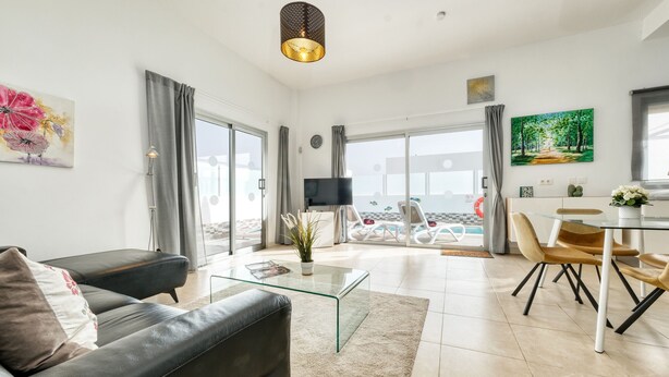 A modern living room with a glass coffee table, a sofa, and a dining area with chairs.