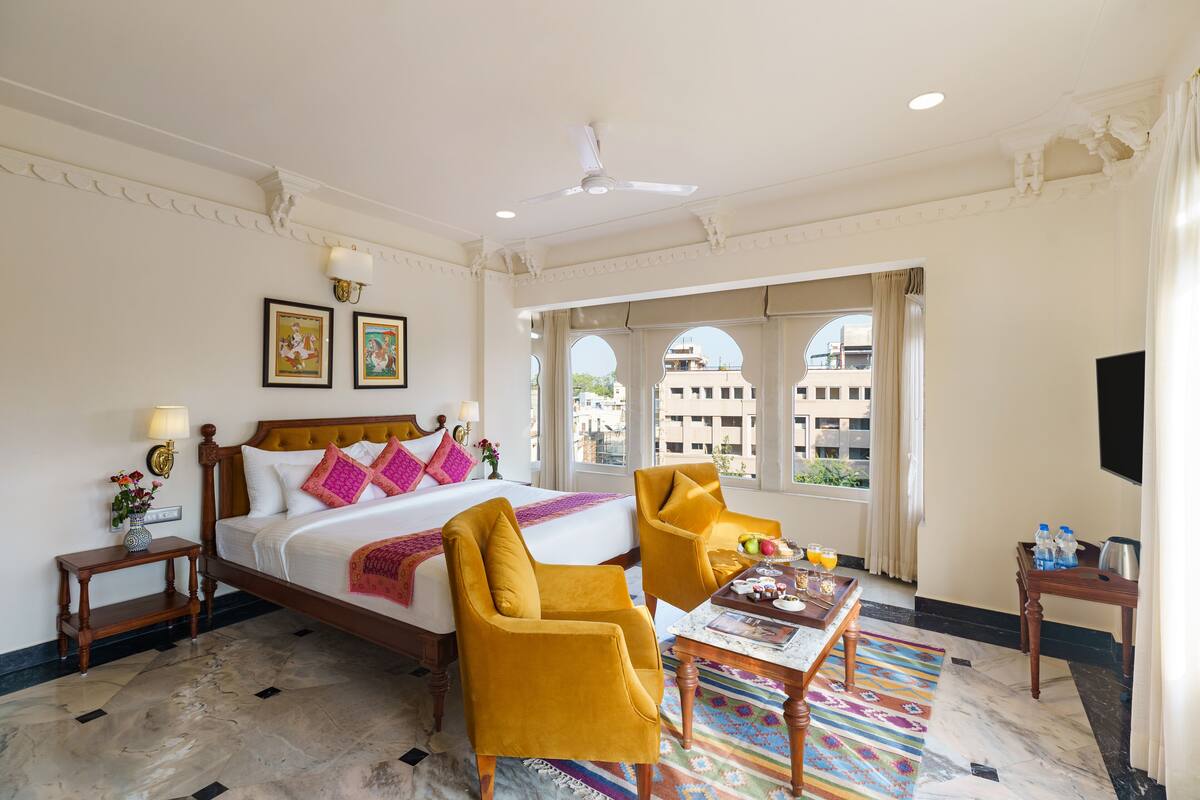 Une chambre d’hôtel comprenant un lit, deux chaises, une table, un téléviseur et une fenêtre donnant sur des immeubles.
