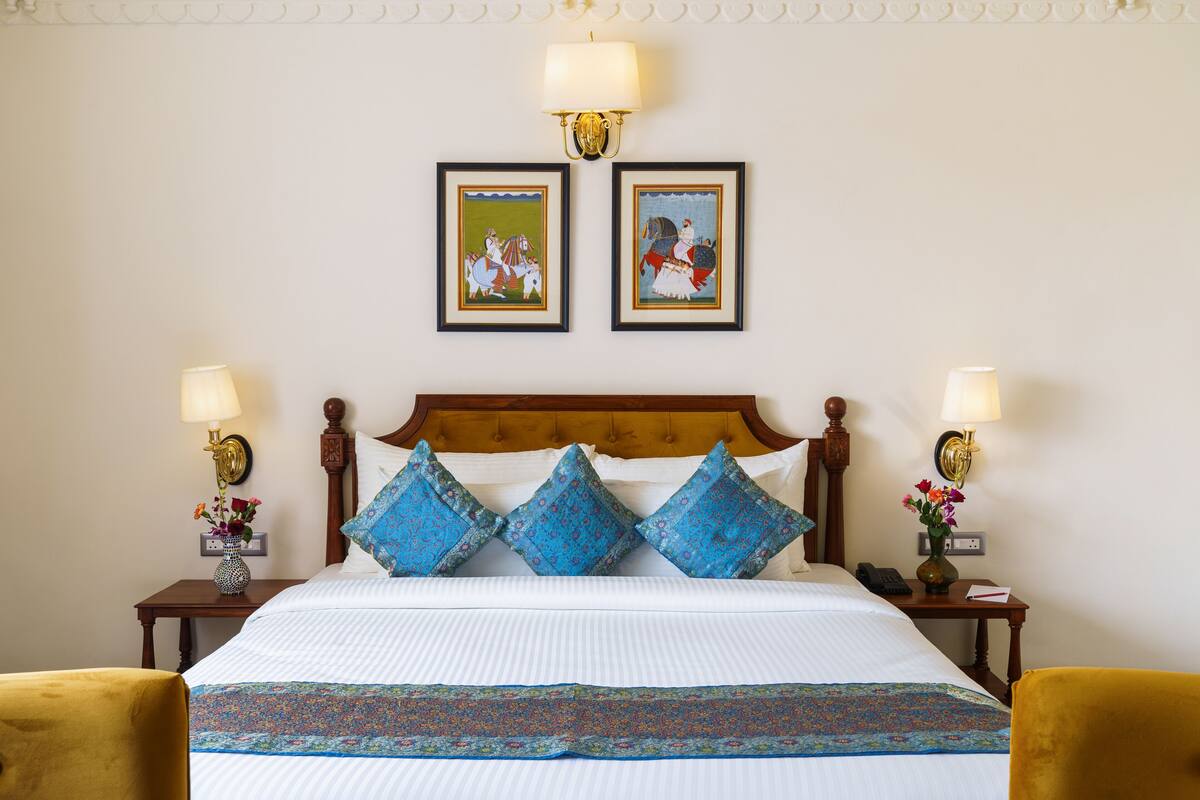 Une chambre d’hôtel avec un grand lit, deux lampes fixées au mur et deux tableaux encadrés au-dessus du lit.