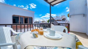 A balcony with a table set for breakfast, including croissants, coffee, and tea.