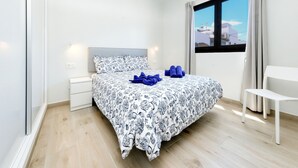 A modern hotel room with a neatly made bed, a bedside table, a chair, and a large window offering a city view.