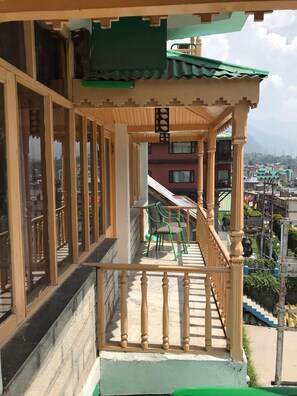 A balcony with wooden railings, a green chair, and a view of a cityscape in the background. - HOTEL EVERGREEN (Manali)