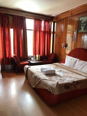 A hotel room with a bed, two chairs, a table, and a window with curtains. - HOTEL EVERGREEN (Manali)