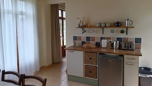 A compact kitchen with a wooden countertop, a refrigerator, and a sink. There are shelves above the counter holding kitchenware and decorative items.