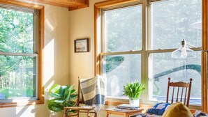 Una habitación acogedora con techo de madera, ventanas amplias, un sofá de cuero, una silla, una mesa con una planta y una lámpara.