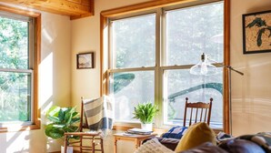 Una habitación acogedora con ventanas amplias, una silla de madera, una mesita y un sofá.