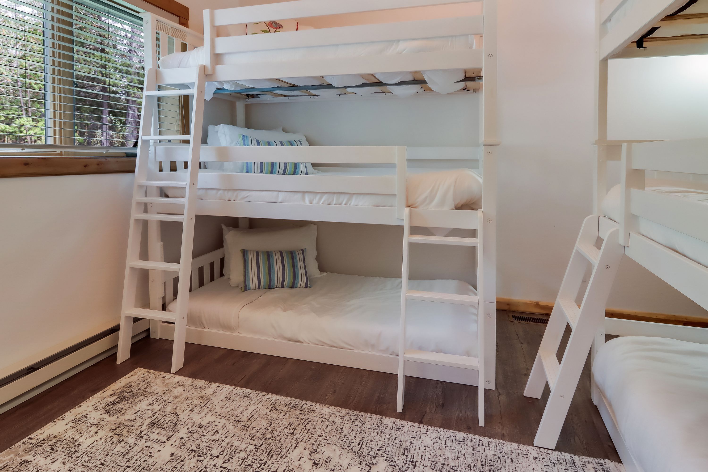 Une chambre avec un lit superposé, une fenêtre, un plancher en bois et un tapis à motifs.