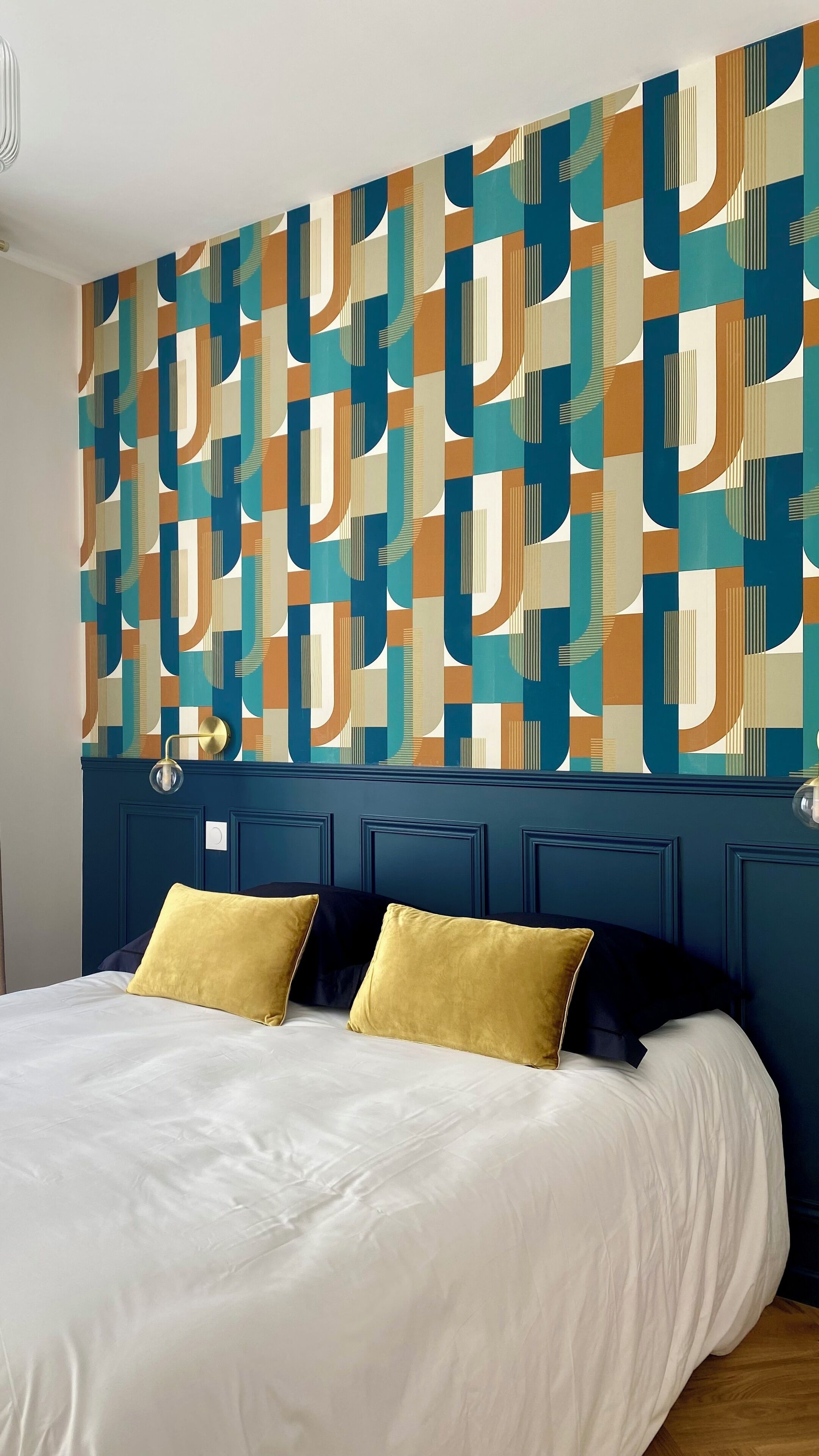 A bedroom with a bed, two yellow pillows, and a geometric patterned wall.