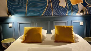 Habitación de hotel con una cama grande, dos almohadas amarillas, una almohada blanca y un mural decorativo en la pared.