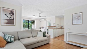 Una sala moderna con un sofá, un comedor con una cocina al fondo y un ventanal que ofrece vistas a zonas verdes.