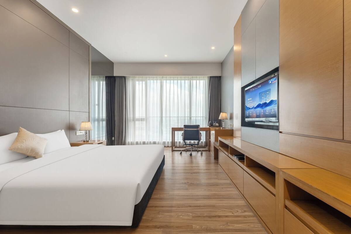 A hotel room with a large bed, a desk with a chair, a TV, and a wooden cabinet.