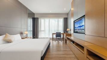 A hotel room with a large bed, a desk with a chair, a TV, and a wooden cabinet.