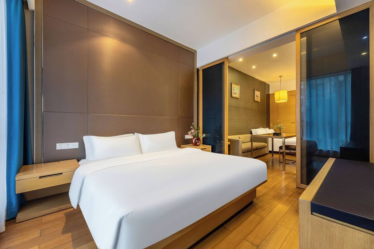 A modern hotel room with a large bed, a desk, a chair, and a small seating area.